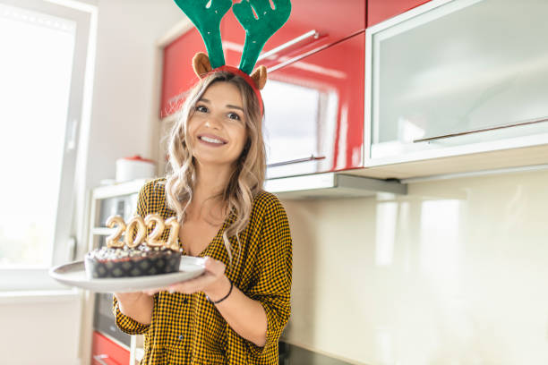 istock Young woman making and decorating chocolate cake with lit candles shaped as numbers 2021 for New Years party 1282549272