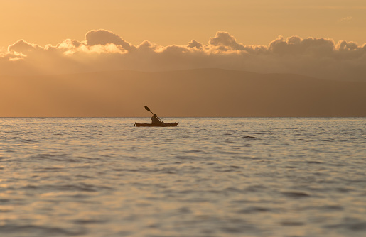 Woman paddling sea kayak at sunset with golden glow