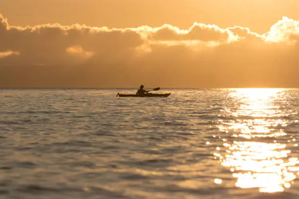 Photo of Woman paddling sea kayak at sunset with golden glow