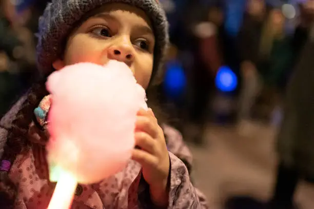 Stock photo of little girl having a cotton candy outside. She is visiting a public event during a winter day in London, UK. This file has a signed model release.