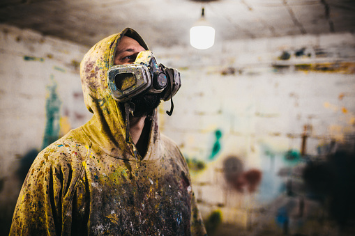 An abstract artist in clothes sprinkled with paint sits in an abandoned room