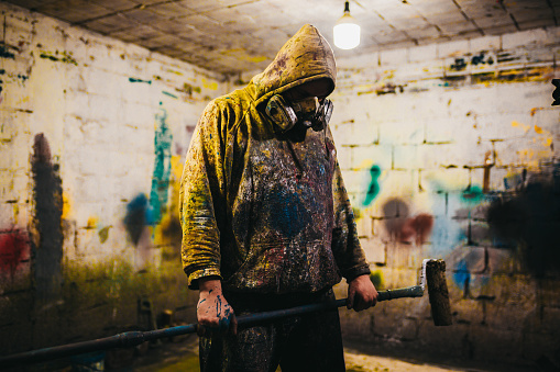 An abstract artist in clothes sprinkled with paint sits in an abandoned room