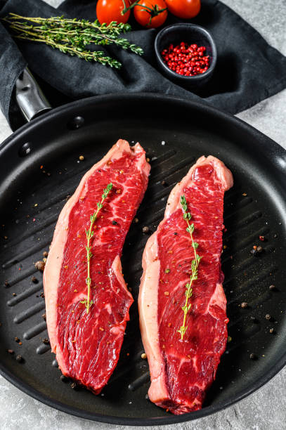 istock Fresh raw sirloin steak on a grill pan. Gray background. Top view 1282551776