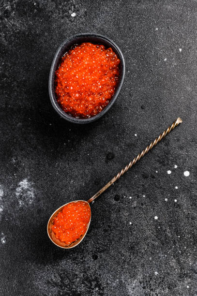 istock Salmon red caviar in an exquisite spoon. Black background. Top view 1282553271