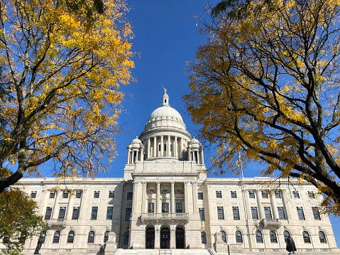 The Rhode Island State House building framed by yellow autumn trees.