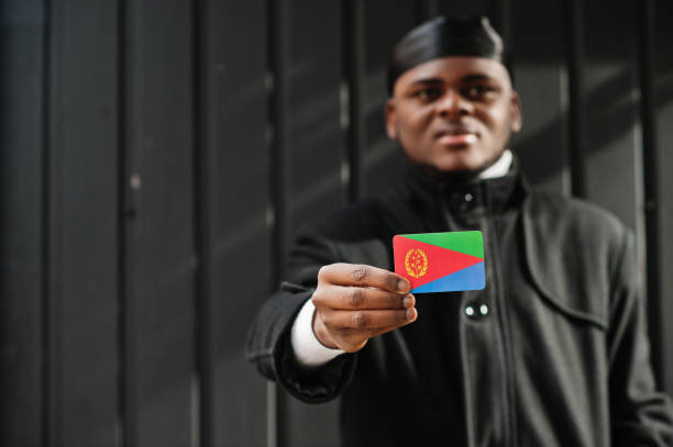 African man wear black durag hold Eritrea flag at hand isolated dark background. African man wear black durag hold Eritrea flag at hand isolated dark background. eritrea stock pictures, royalty-free photos & images