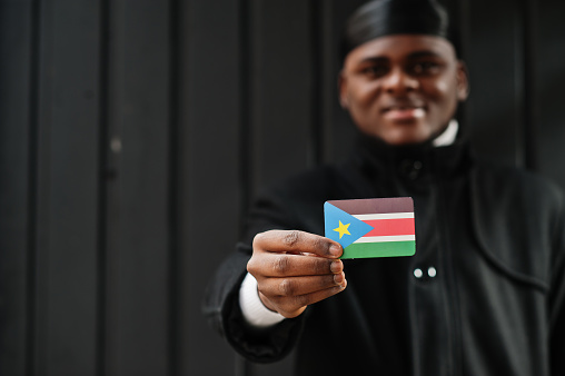 African man wear black durag hold South Sudan flag at hand isolated dark background.