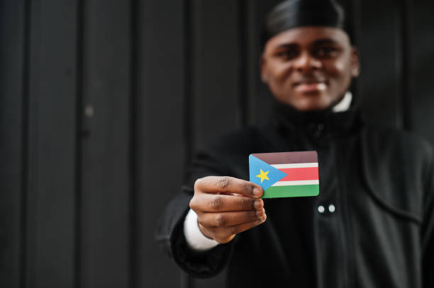 African man wear black durag hold South Sudan flag at hand isolated dark background. African man wear black durag hold South Sudan flag at hand isolated dark background. south sudan stock pictures, royalty-free photos & images