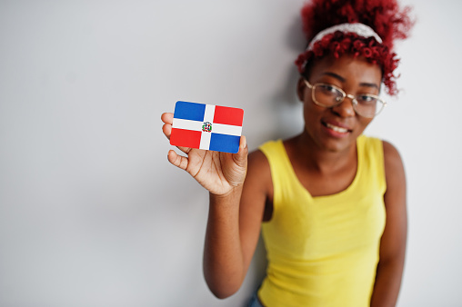African american woman with afro hair, wear yellow singlet and eyeglasses, hold Dominican Republic flag isolated on white background.