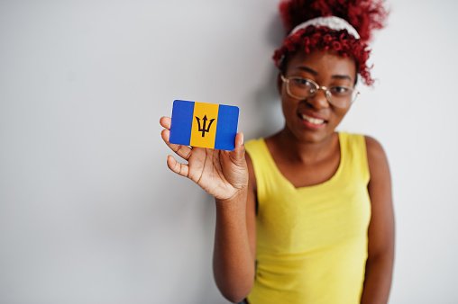 African american woman with afro hair, wear yellow singlet and eyeglasses, hold Barbados flag isolated on white background.