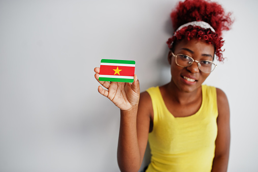African american woman with afro hair, wear yellow singlet and eyeglasses, hold Suriname flag isolated on white background.