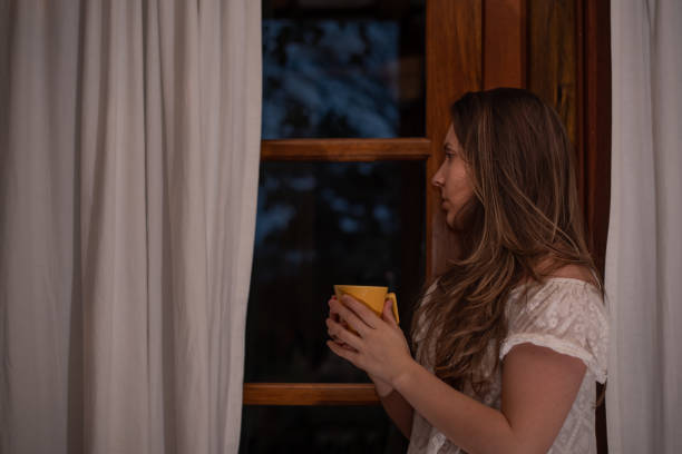 Lonely scared woman looking through the window Woman looking through the window looking out front door stock pictures, royalty-free photos & images