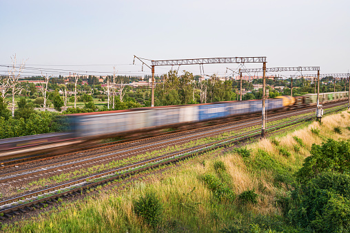 Train with different freight cars that are blurred at high speed on the background of the railway