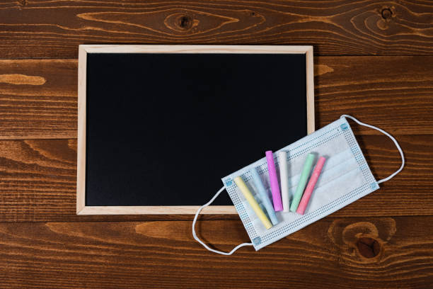 istock A blackboard with space for text, set of colored crayons and a protective mask on a wooden background. Start of school year and sale of school supplies. Home education and learnin after pandemic. 1282558443