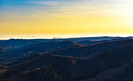 Surreal beautiful nature landscape of mountains and valleys dark jeweled shades under bright yellow sky at sunset