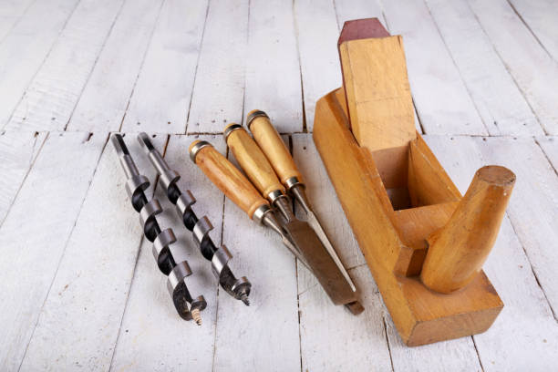 istock Wood planer, chisels and drill bits on a wooden table. Carpentry accessories in a home workshop. Light background. 1282561100