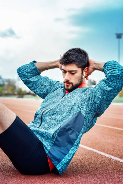 Vertical Shot of a handsome young man doing sit-ups at track and field stadium. Abdominal muscle training stock photo