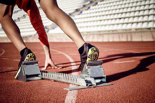 Race track, start blocks and running with athlete feet, run in stadium and ready with action and fitness outdoor. Person training, runner sneakers and sports training with exercise and cardio