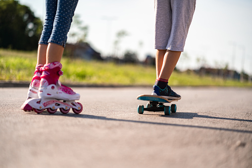 Closeup of a boy riding his skateboard and girl riding her roller skates