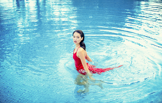 Beautiful asian woman in the pool in a red dress.