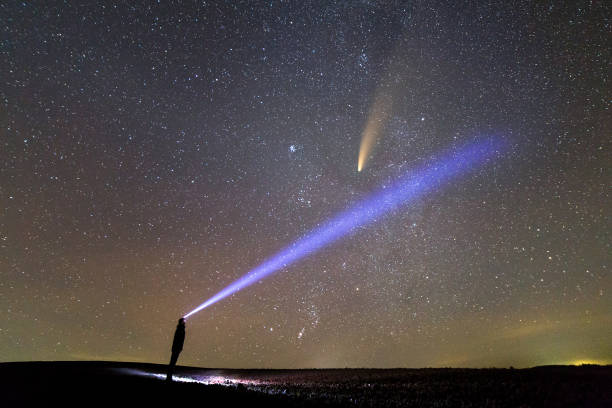 istock Silhouette of a man with flashlight on his head pointing bright beam of light on starry sky with Neowise comet with light tail. 1282565577