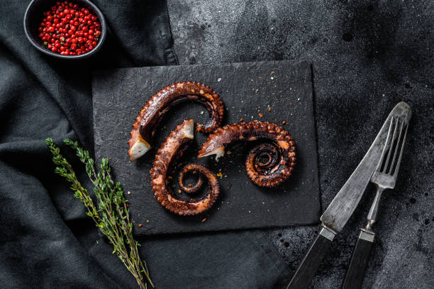 istock Fried octopus tentacles with thyme and pink pepper. Fresh seafood. Black background. Top view 1282568035