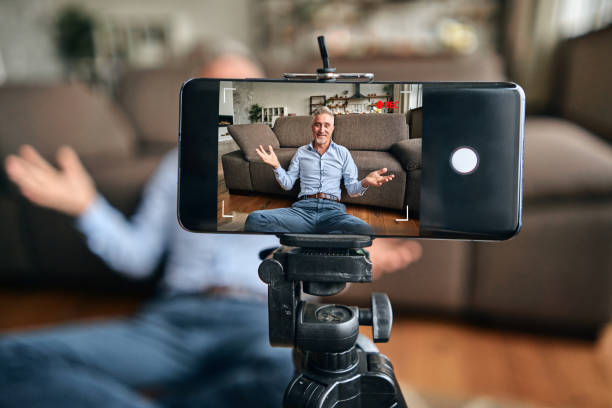 istock Mature man in a blue shirt using smartphone on tripod while making video 1282568054