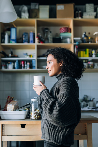 Simple pleasures at home: a beautiful young mixed race woman enjoying a cup of hot tea on a winter morning.