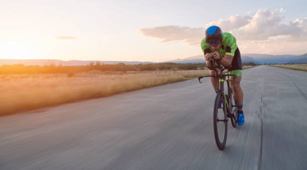 triathlon athlete riding professional racing bike on morning workout sunset or sunrise in background