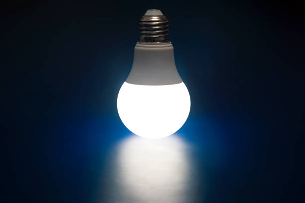 Telephoto image of low energy illuminated lamp reflected on black glass. Incandescent WB.GU10 1 Watt lamp.