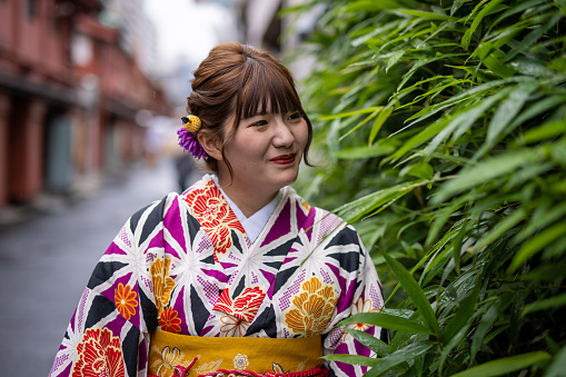 Young woman in kimono looking at bamboo leaves on street