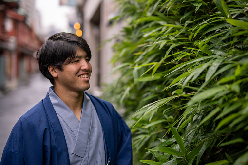 Young man in kimono looking at bamboo leaves on street