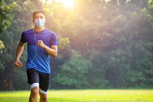 young man in face mask and jogging in the park during quarantine
