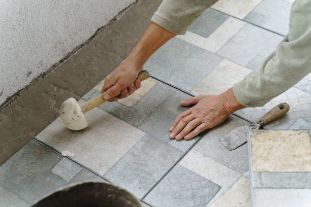 istock Close up on hands of unknown senior man craftsman using hammer to adjust and lay ceramic tiles on the balcony or terrace over adhesive cement in day - construction industry concept copy space 1282588100