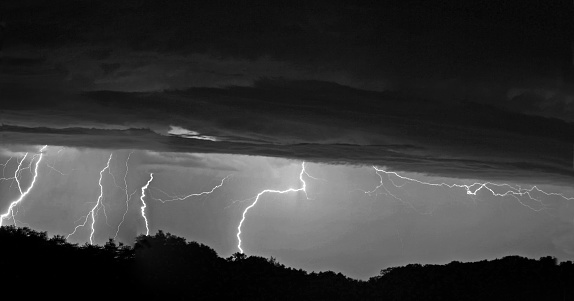 Numerous lightning bolts from clouds striking distant horizon woods, at night. Copy Space, Composite panorama