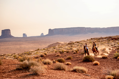 Cuatro jóvenes nativos americanos Navajo hermanos y hermanas montando sus caballos desnudos en el parque tribal del valle del monumento del norte de Arizona al atardecer juntos photo
