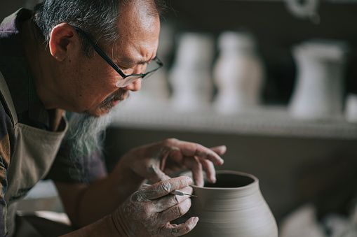 asian chinese senior man clay artist working in his studio with spinning pottery wheel
