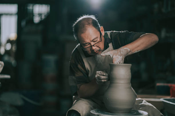 asiatico cinese senior uomo argilla artista che lavora nel suo studio con ruota di ceramica rotante - shaping clay foto e immagini stock