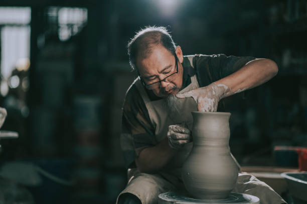 陶器の輪を紡いで彼のスタジオで働くアジアの中国の先輩粘土アーティスト - shaping clay ストックフォトと画像
