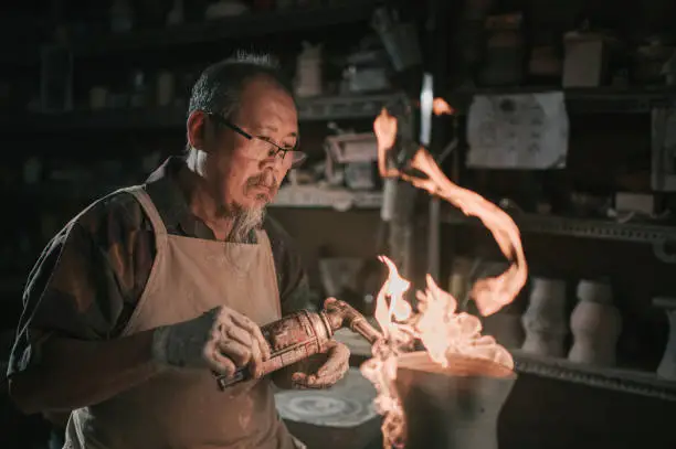 asian chinese senior man clay artist working in his studio with blow torch on his art craft