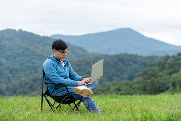 istock Asian man sitting on the chair using laptop computer with internet for online working or video conference on the mountain. Handsome guy relax and enjoy outdoor lifestyle in autumn holiday vacation. 1282598752