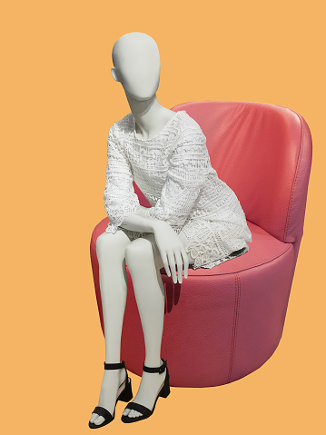 Female mannequin sitting on a red leather chair, isolated. No brand names or copyright objects.