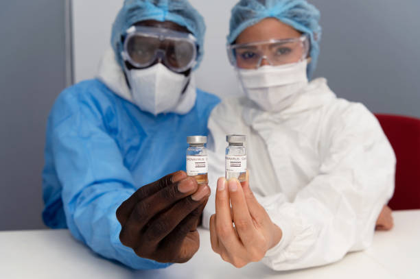 istock Coronavirus covid 19 disease experts hold samples of coronavirus covid 19 vaccine sample labelled coronavirus covid 19 with confidence and protective suit, mask and gloves 1282606025