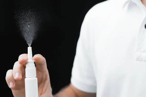 A man in a white shirt on a black background checks the nasal spray.