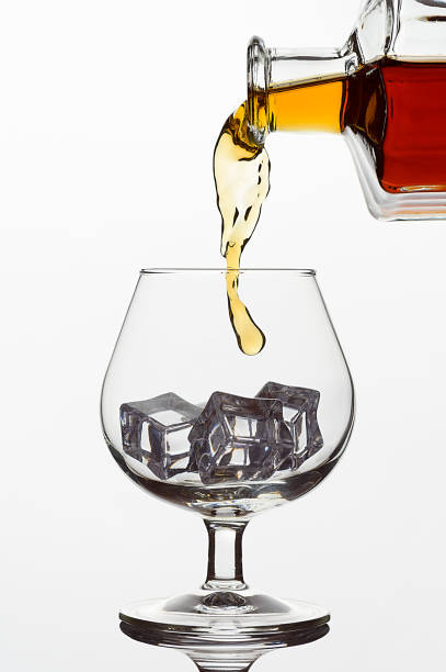 氷の立方体が付いた透明なガラス。白い孤立した背景にウイスキーやコニャックやブランデーのボトルから冷凍ストリーム - whisky alcohol pouring glass ストックフォトと画像