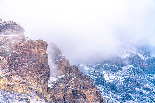 The rocky and steep slope of Provo Canyon in Utah blanketed with hazy clouds. The precipitous canyon is dusted with snow on this cloudy winter day.