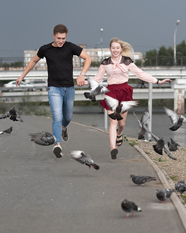 Couple in love holding hands run with pigeons on the street in the city
