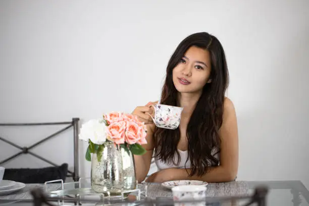 Picture of a Chinese woman drinking coffee in the living room with flowers.