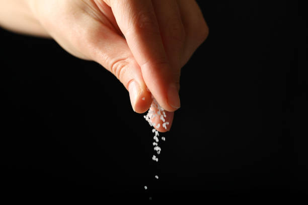 istock Female hand adding salt on black background 1282623319