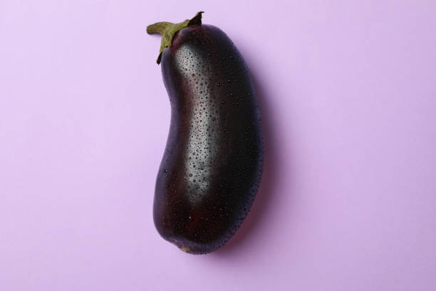 istock Fresh raw eggplant with water drops on violet background 1282623746